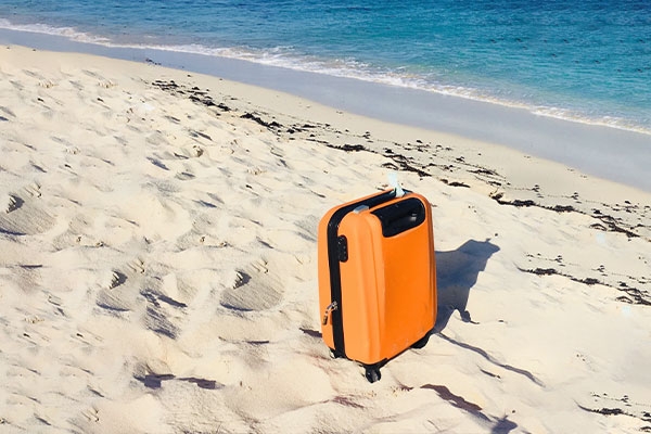 Mala laranja de viagem na beira da praia