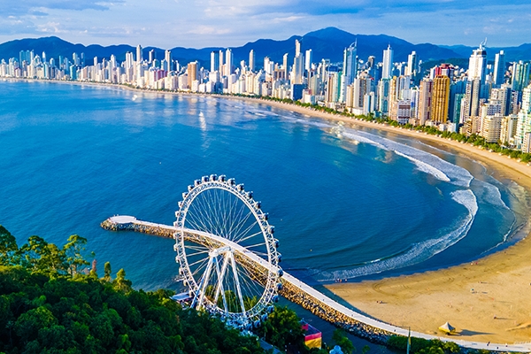 Imagem de Balneário Camboriú vista de cima. Respectivamente, seus prédios, praia e roda gigante.